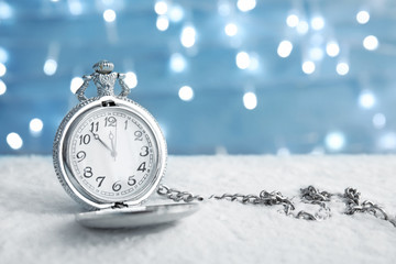 Fototapeta na wymiar Pocket watch with snow on table against blurred lights. Christmas countdown