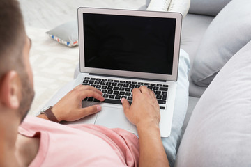 Naklejka premium Man in casual clothes using laptop on sofa at home
