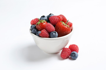 Bowl with raspberries, strawberries and blueberries on white background