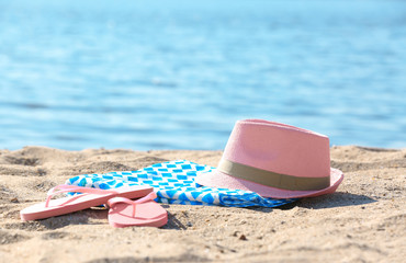 Bright towel, hat and flip flops on sand near sea. Beach object