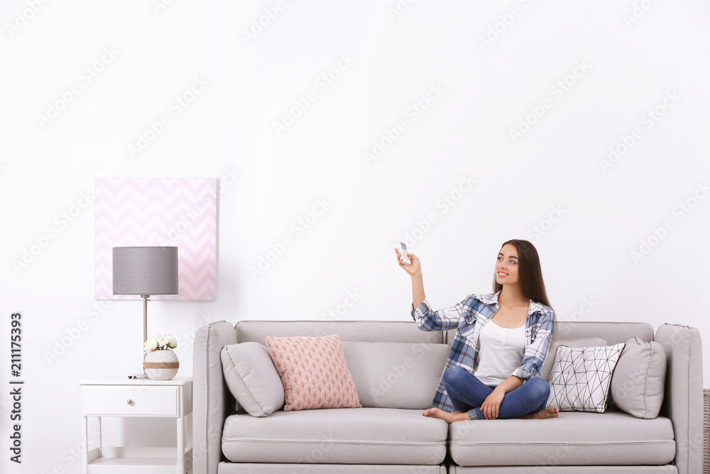 Canvas Prints young woman switching on air conditioner while sitting on sofa near white wall