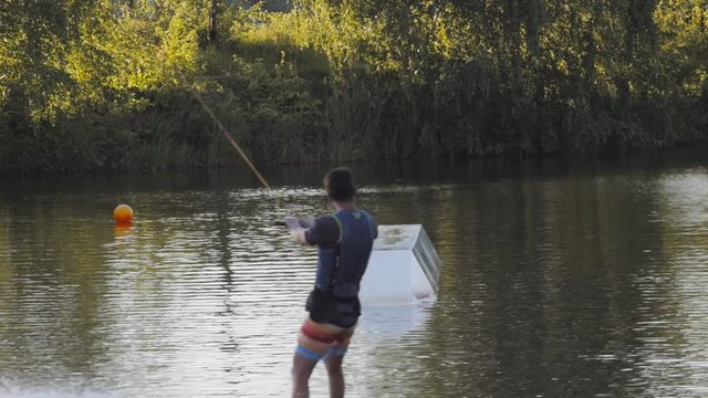 Wakeboarder ride on cable wakeboard in park, outdoor extreme slow motion on water, surfing athlete on water doing boardslide, noseslide or tailslide 180 out, backside bluntslide