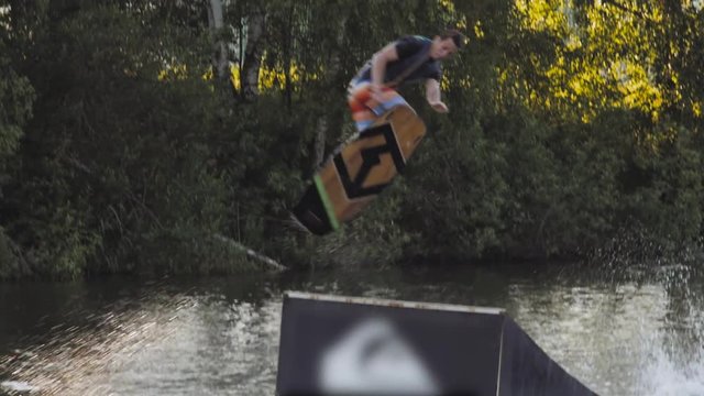 Wakeboarder ride on cable wakeboard in park, outdoor extreme slow motion on water, surfing athlete on water doing boardslide, noseslide or tailslide 180 out, backside bluntslide