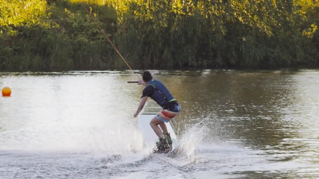 Wakeboarder ride on cable wakeboard in park, outdoor extreme slow motion on water, surfing athlete on water doing boardslide, noseslide or tailslide 180 out, backside bluntslide