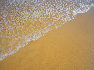 Close up photo from top view of wave foam coming to the beach. Sand with coming up water, diagonal