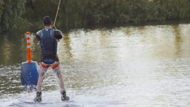 Wakeboarder ride on cable wakeboard in park, outdoor extreme slow motion on water, surfing athlete on water doing boardslide, noseslide or tailslide 180 out, backside bluntslide