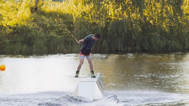 Wakeboarder ride on cable wakeboard in park, outdoor extreme slow motion on water, surfing athlete on water doing boardslide, noseslide or tailslide 180 out, backside bluntslide
