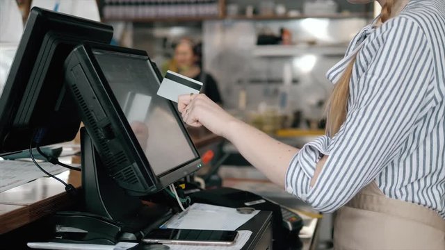 Side view of young bartender using modern cash register at bar counter