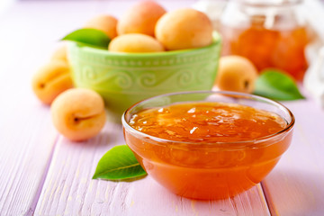 Apricot jam in glass bowl and fresh apricots on light purple wooden background