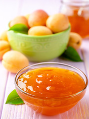 Apricot jam in glass bowl and fresh apricots on light purple wooden background