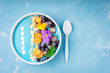 Blue smoothie bowl with fruits, berries, nuts and flowers. Tropical healthy smoothie dessert. Healthy food, vegetarian, diet concept. Top view. Copy space