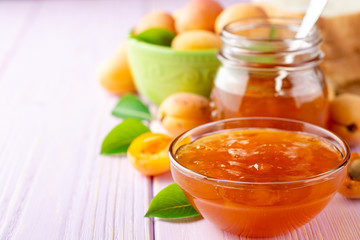 Apricot jam in glass bowl and fresh apricots on light purple wooden background