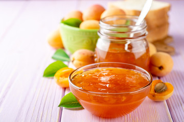 Apricot jam in glass bowl and fresh apricots on light purple wooden background
