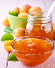Apricot jam in glass bowl and fresh apricots on light purple wooden background