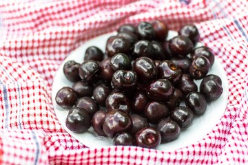Dark crimson cherry on plate on red towel.