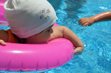 Portrait of happy white Caucasian child baby girl toddler in swimming pool outdoor. Preschool boy training to float with pink inflatable circle ring in water. Healthy active lifestyle. summer, joy