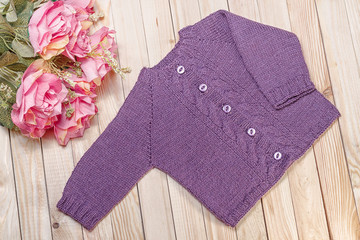 knitted baby jacket of blackberry color on a light wooden background