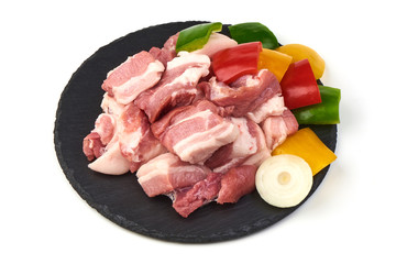 Pieces of fresh pork meat sliced vegetables on stone plate, isolated on white background. Close-up.