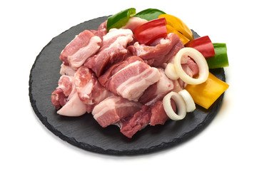 Pieces of fresh pork meat sliced vegetables on stone plate, isolated on white background. Close-up.