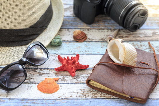 Summer concept with hat, camera, sunglasses, diary, and seashells side view
