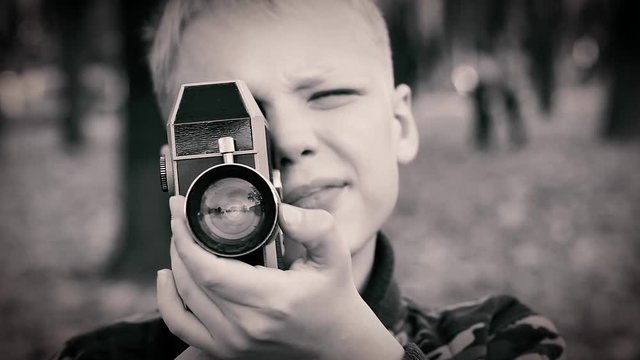 Cute little blond kid using old retro film camera to shoot video. Filtered in vintage style. Real time full hd video footage.