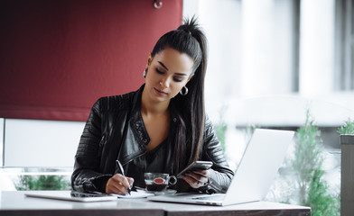 Beautiful girl working out a plan of the project and concept. Girl paints a website design on a laptop. student prints a message on the phone in the messenger. Development. Digital marketing