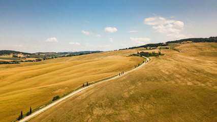 Fototapeta na wymiar Typical countryside summer landscape in Tuscany, Italy. Road through a wheat field. Aerial view by drone.