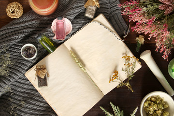 An open empty vintage notebook surrounded by herbs, alchemy appliances, potions and ingredients lies on a dark wooden table. Magic alchemy and occultism. Flat lay with copy space for text. Mock up