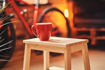 Minimalism concept. Close-up image of a red cup on a wooden stool on a room with a loft interior.
