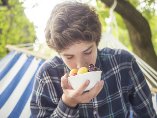 young teenage boy smell fresh fruit and berry plate lying on hammock