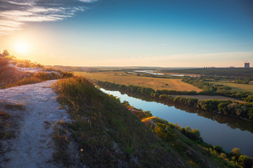 Obraz premium Beautiful nature landscape panorama at sunset time. View from chalk hill or mountain to green meadows and fields with river and nuclear power plant far away. Summer travel tranquil background