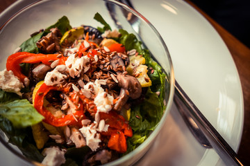 Glass bowl of healthy roasted vegetables salad on a wooden table. Low key food photography, warm toned filter