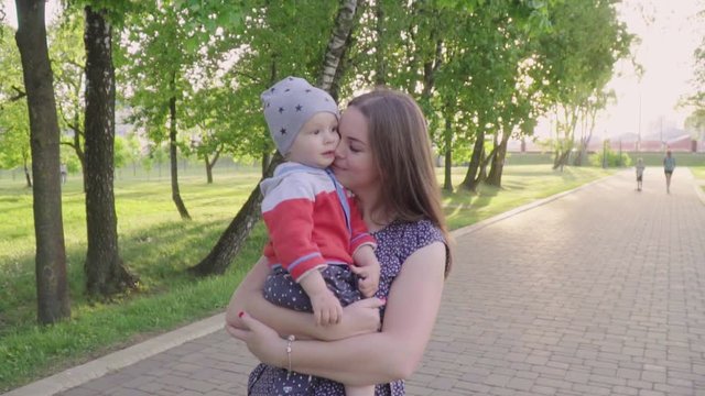 Young mother with her little son relaxing and playing in the park, hugging and kissing son, weekend together, lazy morning, warm and cozy scene. slow mo