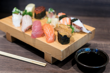 Close-up sushi and sashimi mixed on wooden plate on black wooden table. Japanese food.