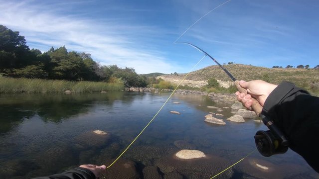 First person scene of man flyfishing casting in Pulmari river, in Neuquen, Patagonia Argentina on a sunny and windy day. River full of big rounded rocks.