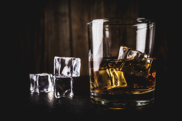 Two whiskey shot glasses on dark wooden background, with ice cubes, copy space
