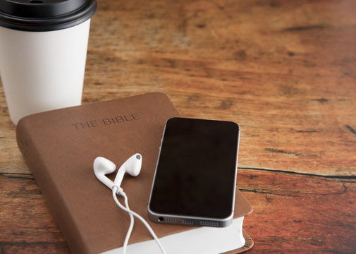 Physical Bible and a Smart Phone with Earphones on a Wood Table