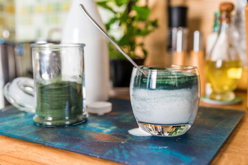 Closeup view fresh kefir probiotik drink in clear glass and spoon with green spirulina powder ready to mix on kitchen table