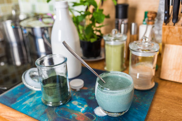 Obraz na płótnie Canvas Closeup view fresh kefir probiotik drink in clear glass mixed with green spirulina powder on kitchen table