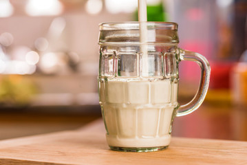 Closeup view pouring fresh kefir probiotik drink into half full clear glass cup on kitchen table