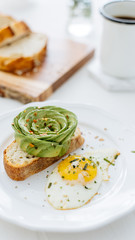 Breakfast setting featuring avocado rose on toast, sunny side up egg and coffee.