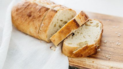 Loaf of bread sliced on wood cutting board and white linen.
