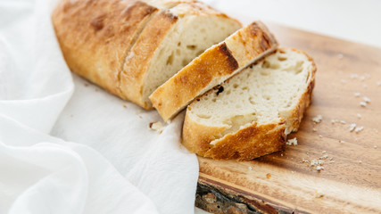 Loaf of bread sliced on wood cutting board and white linen.