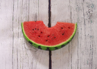 Slice of watermelon with bite on a white wooden background