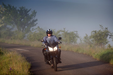 man riding a motorbike on foggy road in early morning