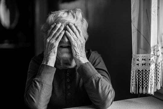 Elderly woman covered her face with both hands. Black and white photo.