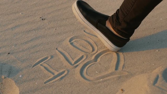 The inscription on the sand "I love", on which the foot steps. close - up, slow motion.