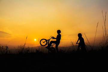 Fototapeta na wymiar silhouette of two little girl riding bicycle at sunset, kids sport and active lifestyle