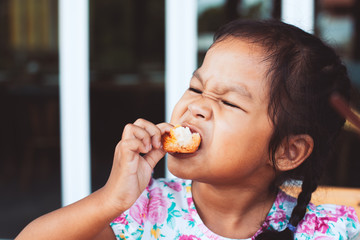 Cute asian little child girl eating delicious toast for breakfast with happiness