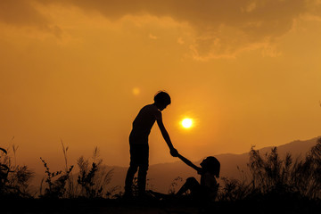 silhouette of little girl helping sister at sunset time,